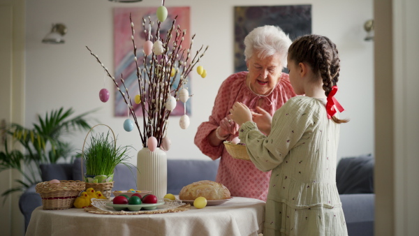 Grandmother with granddaughter setting table for traditional easter lunch. Recreating family traditions and customs. Concept of family easter holidays. Standing by table, praying.