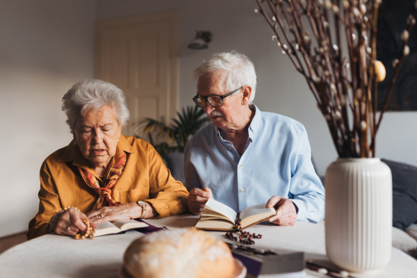 Senior couple praying during Easter, the Bible on table at home. Preparing for church serice. Easter as religious holiday in Christianity.