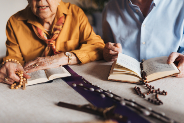 Senior couple praying during Easter, the Bible on table at home. Preparing for church serice. Easter as religious holiday in Christianity.