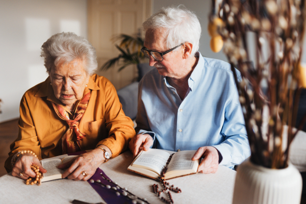 Senior couple praying during Easter, the Bible on table at home. Preparing for church serice. Easter as religious holiday in Christianity.