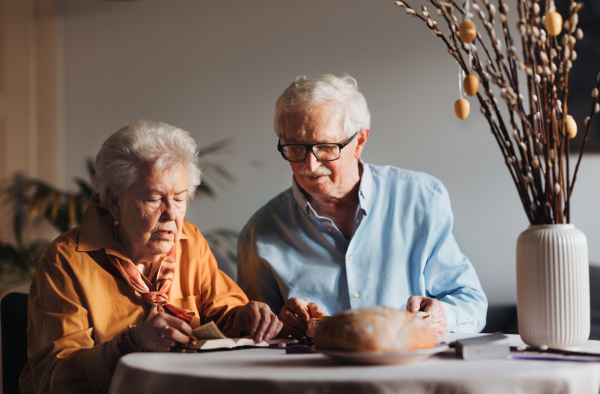 Senior couple praying during Easter, the Bible on table at home. Preparing for church serice. Easter as religious holiday in Christianity.