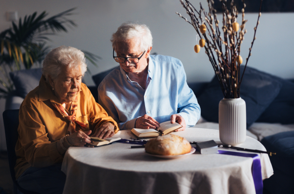 Senior couple praying during Easter, the Bible on table at home. Preparing for church serice. Easter as religious holiday in Christianity.