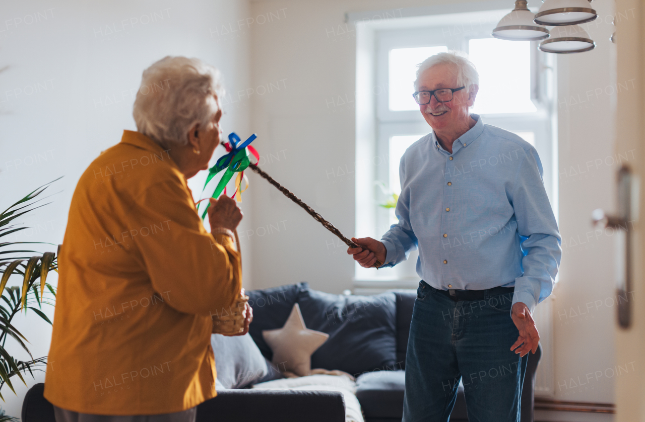 Senior man holding handmade whip, gently whipping elderly woman and speaking tranditional verses and easter wishes. Easter tradition, whip made of willow branches, decorated with ribbons. Unique easter custom from slovakia.