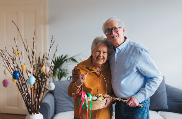 Portrait of senior couple holding handmade whip and basket with colored easter eggs. Easter tradition, unique easter custom from slovakia. Easter tradition, whip made of willow branches, decorated with ribbons. Unique easter custom from slovakia.