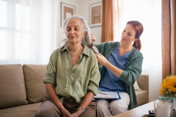 Nurse spending quality time with senior woman at her home, combing her beautiful hair. Female caregiver taking care of elderly patient.