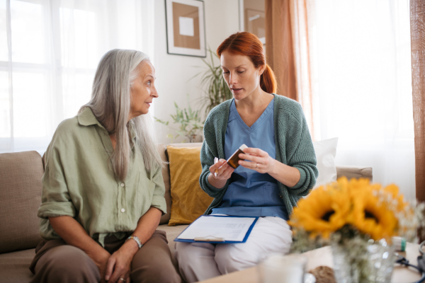 Nurse giving pills to senior woman in her home.