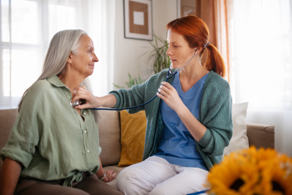 Nurse examining senior patient with stethoscope at home.