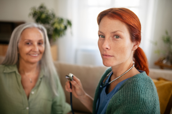 Nurse examining senior patient with stethoscope at home.