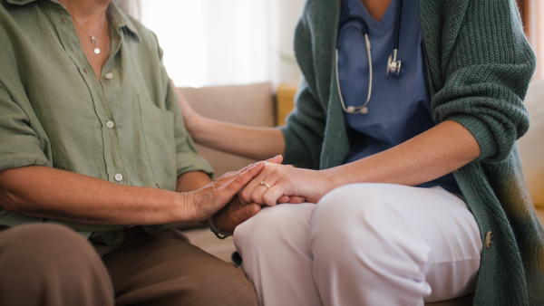 Close-up of caregiver holding hand to senior client.