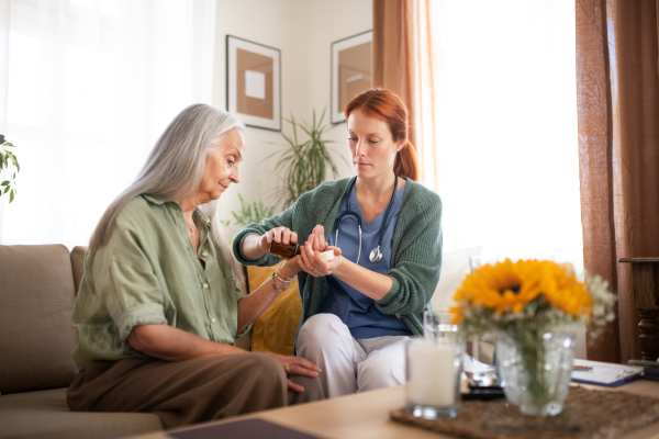 Nurse explaining senior woman how to take medicine. Female caregiver taking care of elderly patient.