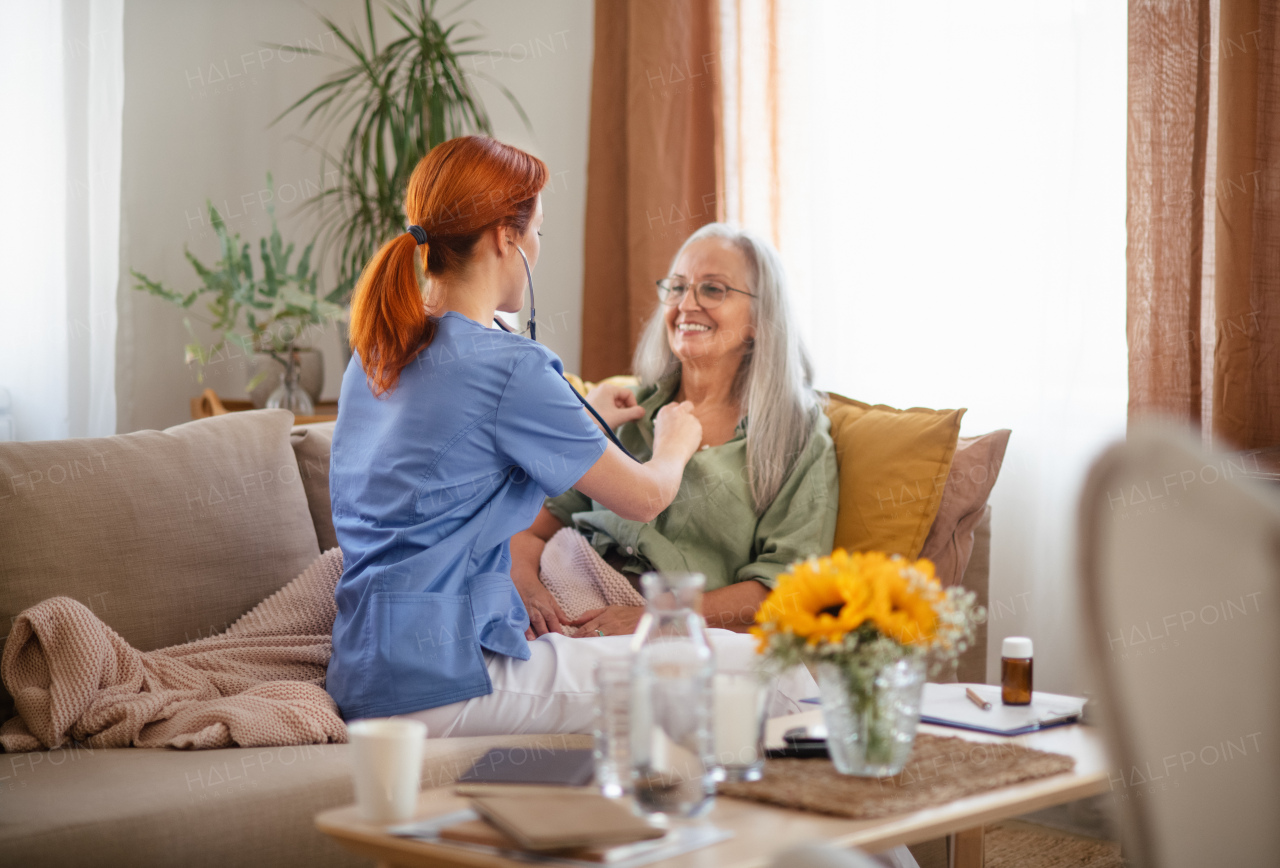 Nurse examining senior patient with stethoscope at home.