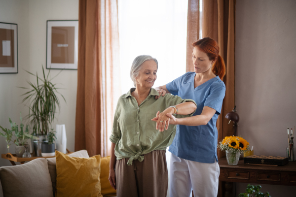 Nurse exercising with senior woman at her home, concept of a healthcare and rehabilitation.