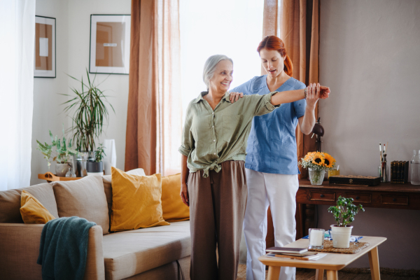 Nurse exercising with senior woman at her home, concept of a healthcare and rehabilitation.