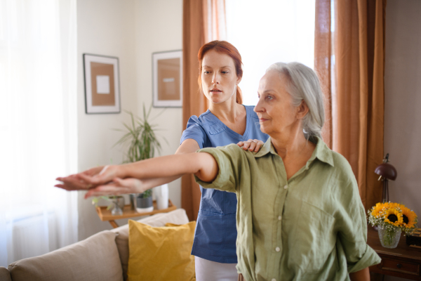 Nurse exercising with senior woman at her home, concept of a healthcare and rehabilitation.