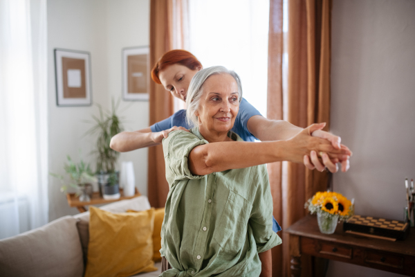 Nurse exercising with senior woman at her home, concept of a healthcare and rehabilitation.