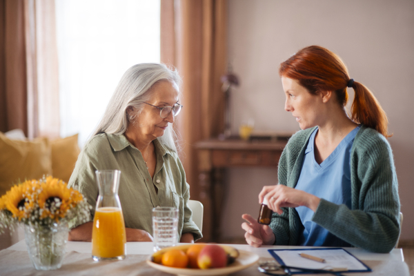 Nurse explaining senior woman how to take medicine. Female caregiver taking care of elderly patient.