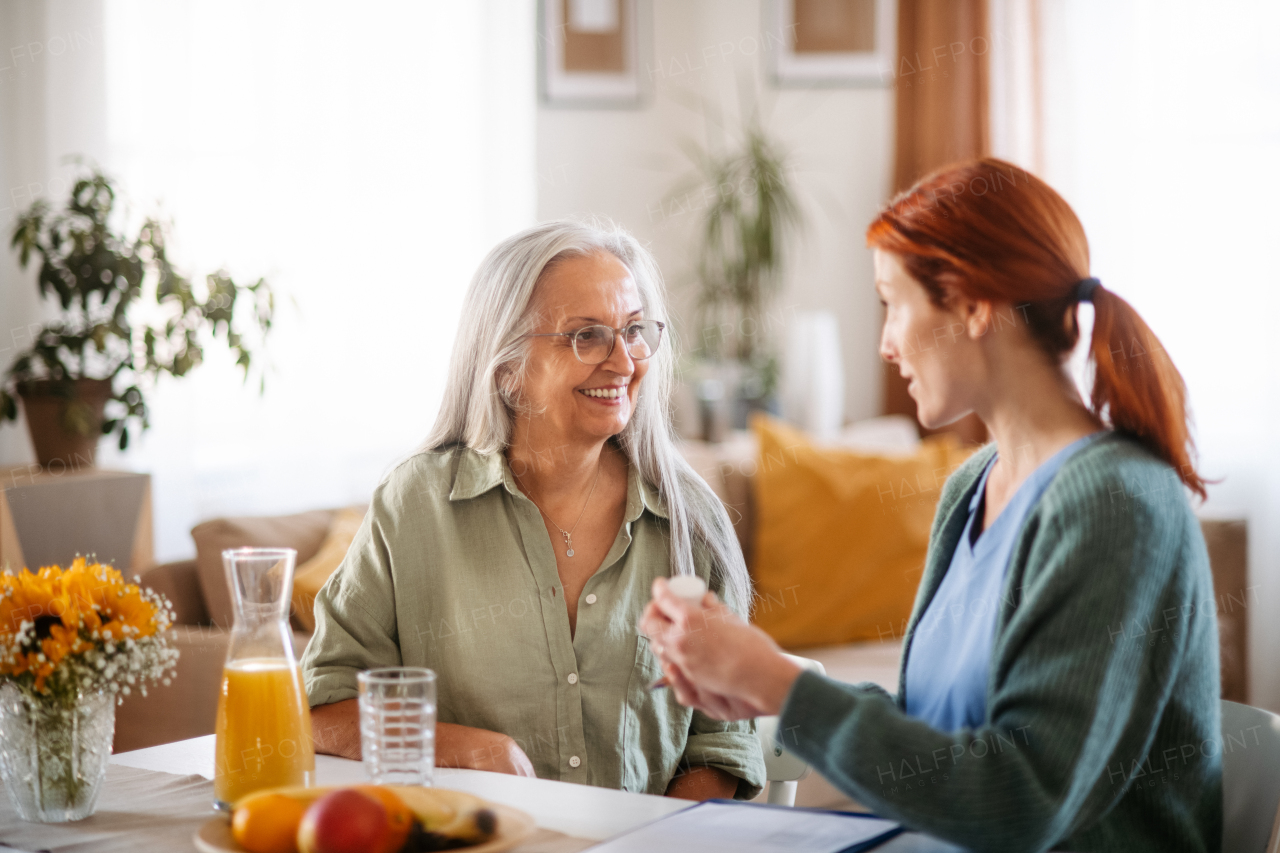 Nurse giving pills to senior woman in her home.