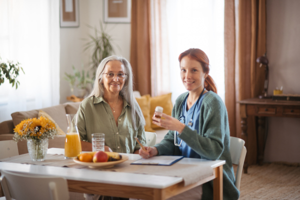 Nurse explaining senior woman how to take medicine. Female caregiver taking care of elderly patient.