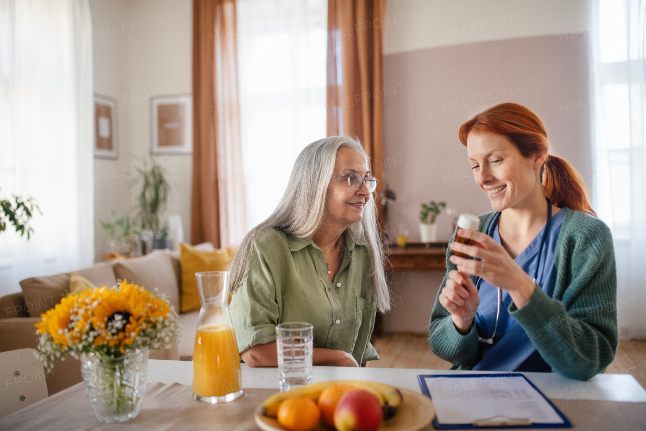 Nurse giving pills to senior woman in her home.