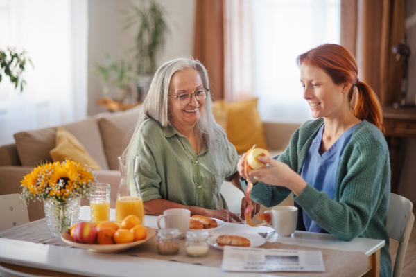 Cregiver preparing breakfast for a senior client in a bed.