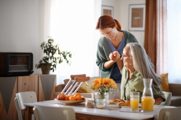 Nurse helping senior woman with walking after leg injury, in her home.