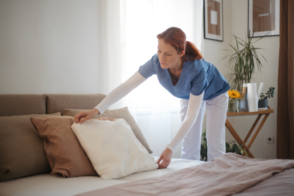 Nurse making the bed in the patient's room. Female caregiver taking care of elderly patient.