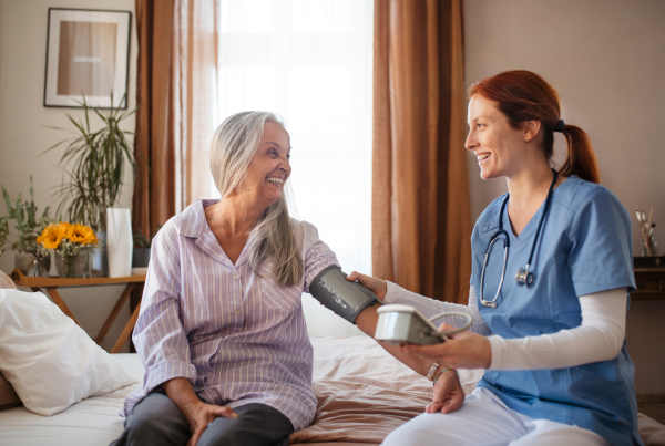 Nurse measuring an elderly woman's blood pressure at home. Female caregiver taking care of senior patient. Check-up after surgery.