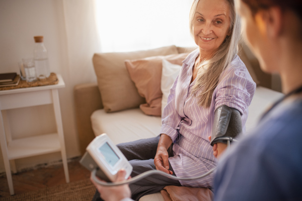 Nurse measuring blood pressuer to senior woman in her home.