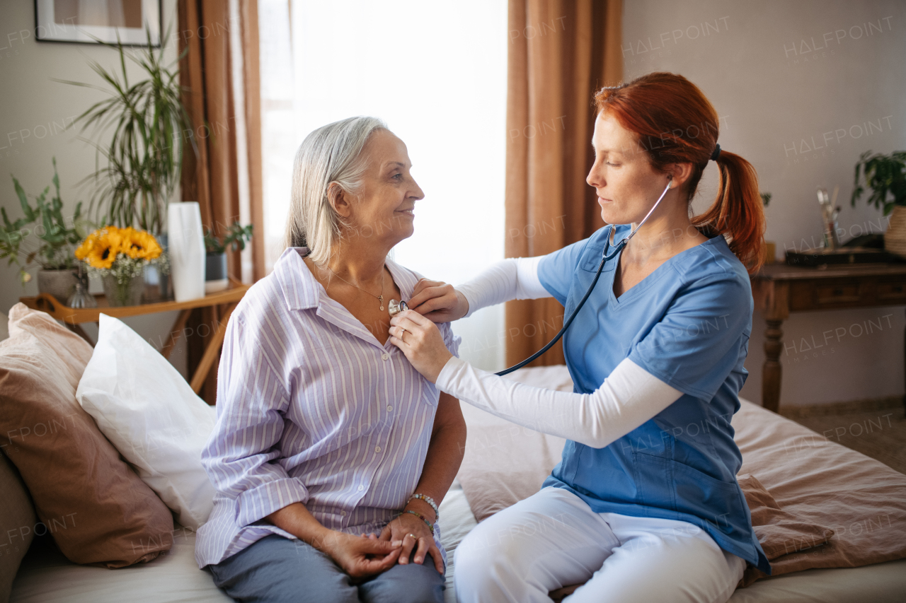 Nurse examining senior patient with stethoscope at home.