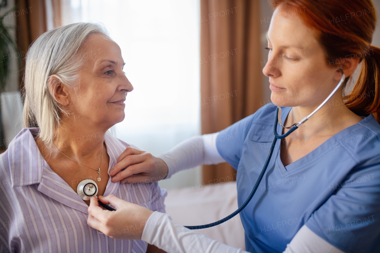 Nurse examining senior patient with stethoscope at home.