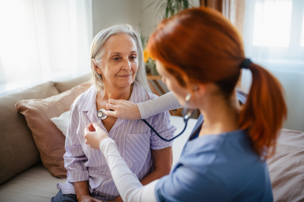 Nurse examining senior patient with stethoscope at home.