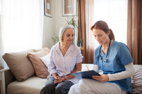 Female caregiver doing regular check-up of senior client in her home. Nurse taking care of senior patient.