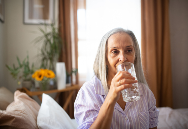 Portrait of senior woman sitting on the bed in a pajamas and drinking water.