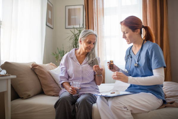 Nurse explaining senior woman how to take medicine. Female caregiver taking care of elderly patient.