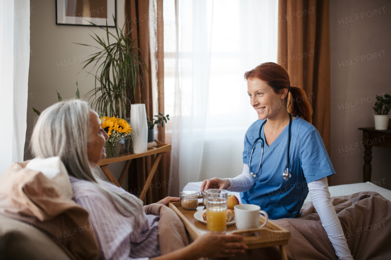 Nurse serving food in the bed to a lying patient at her home. Senior woman eating breakfast in bed after surgery. Female caregiver taking care of elderly patient.