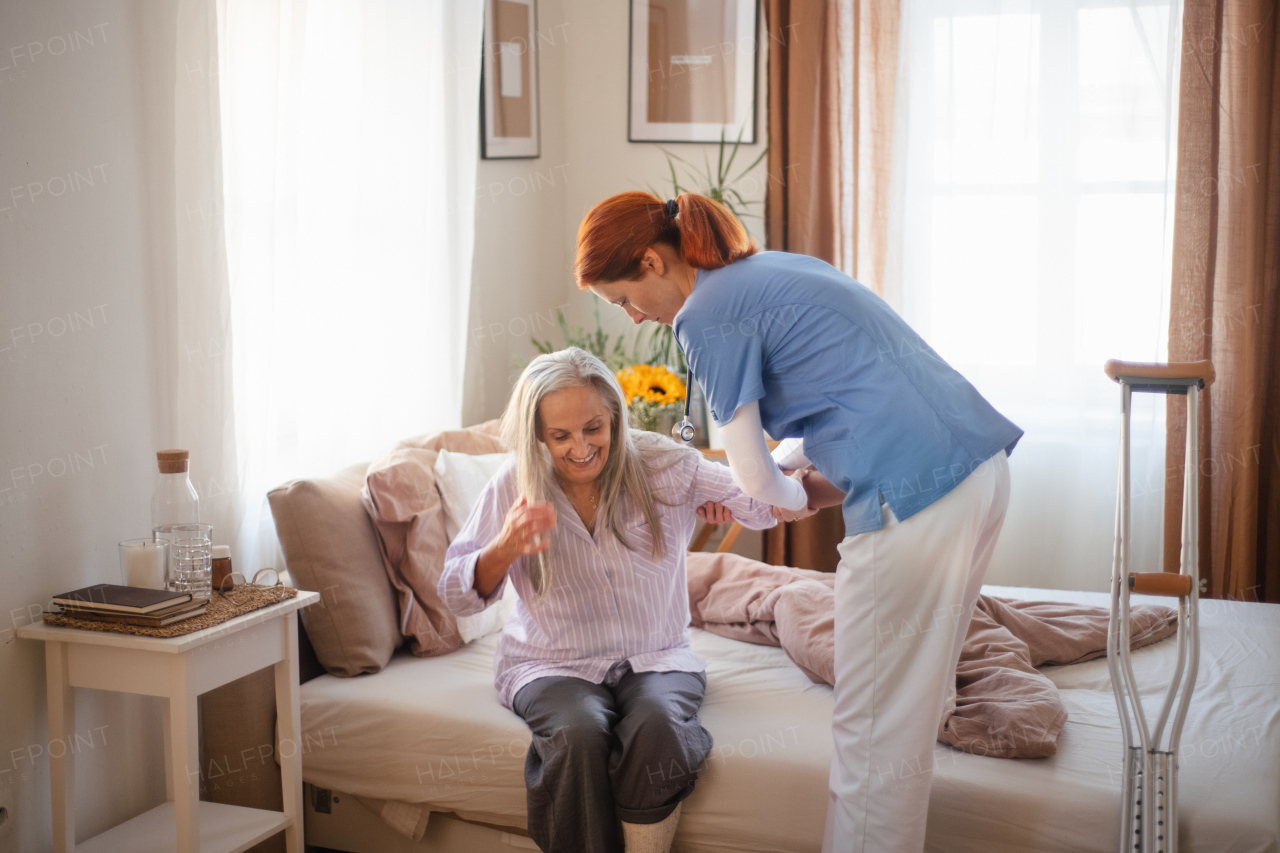 Nurse helping senior woman with walking after leg injury, in her home.