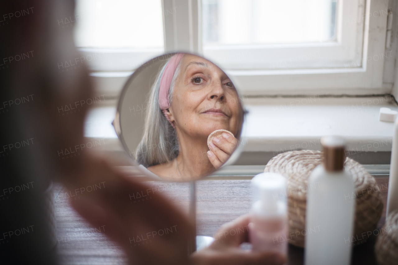 Senior woman making make up herself in home. Skincare routine of beautiful elderly woman. Reflection in the beauty mirror.