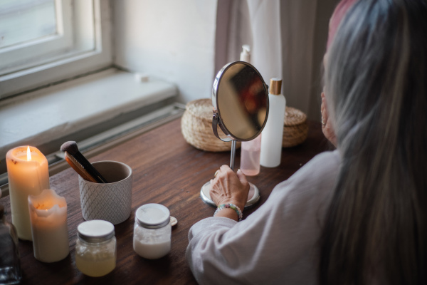 Rear view of senior woman making make up herself in home.