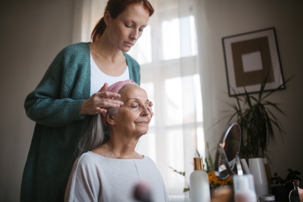 Mature daughter giving facial massage to her mother. Nurse spending quality time with senior woman at her home, giving her gentle facial massage.