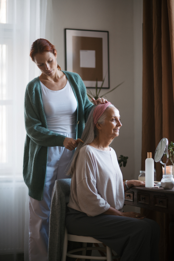 Nurse spending quality time with senior woman at her home, combing her beautiful hair. Mature woman taking care of her elderly mother.