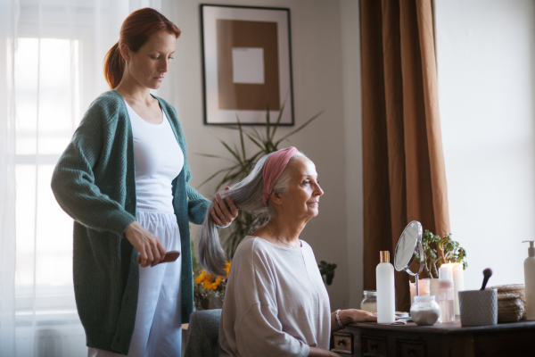 Nurse spending quality time with senior woman at her home, combing her beautiful hair. Mature woman taking care of her elderly mother.