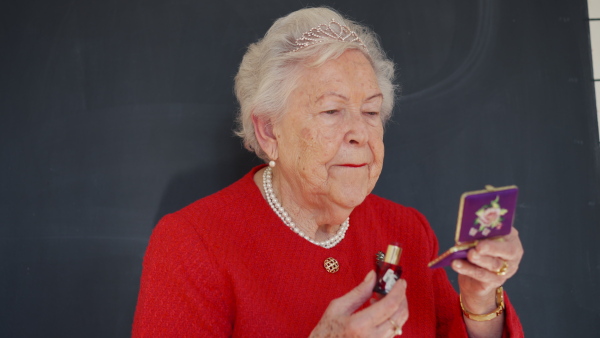 A video of elegant elderly woman with crown applying red lipstick on lips, smiling. Queen lookalike.