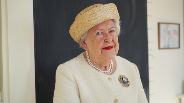 A video of elegant elderly woman in white jacket and hat, looking at camera, smiling. Queen lookalike.