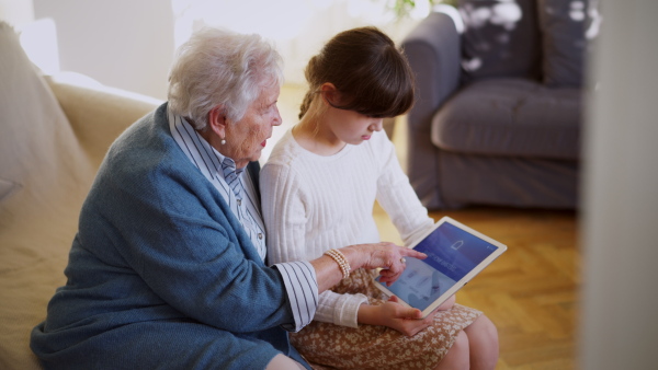 A girl teaching grandmother work with smart thermostat. Adjusting household functions, lighting, security cameras, door locks and thermostat or heating settings on tablet. Elderly people and smart home.