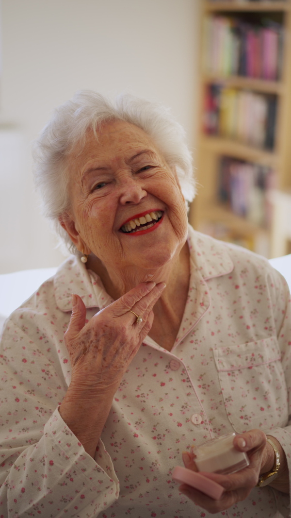 A skincare routine for senior woman. Applying moisturiser cream on face, smiling.