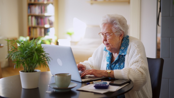 A senior woman reading notification about increased healthcare costs, bad medical test results, high utility bill. Elderly woman working on laptop, shopping online, risk of frauds and hoax for elderly people.