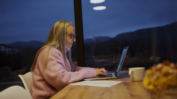 A senior woman sitting indoor and working on laptop.