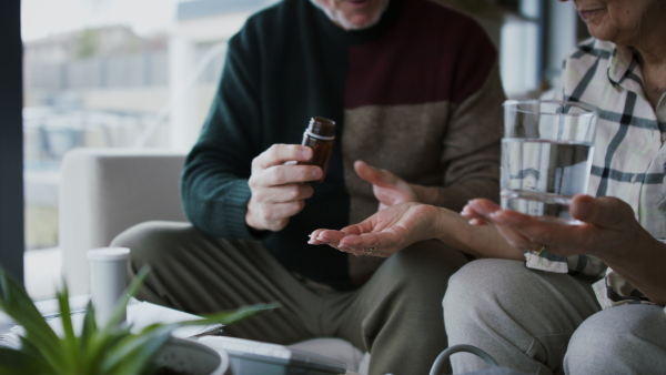 A close-up of senior man giving his wife medication at home