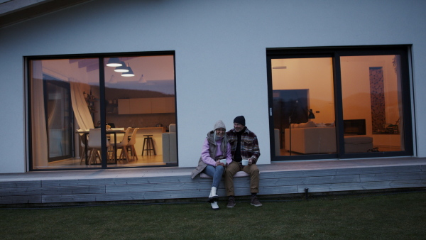 A happy senior couple sitting on terrace and drinking coffee together.