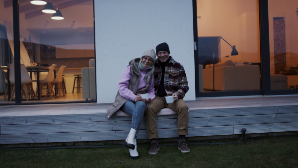 A happy senior couple sitting on terrace and drinking coffee together.